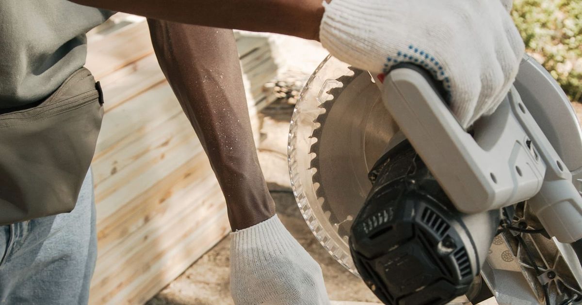 Carpenter cutting a timber board with a saw outdoors
