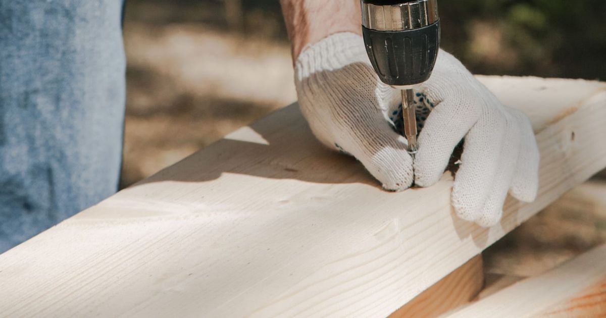 Gloved hands using a cordless drill with its battery pack attached