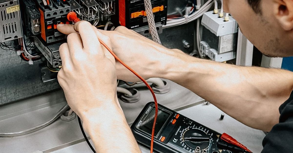 Electrician testing connections in an open switchboard with a multimeter