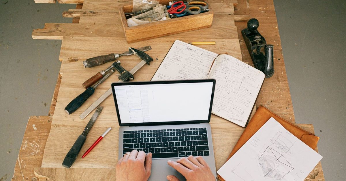 Tradie using a laptop on a timber workbench covered in tools and plans