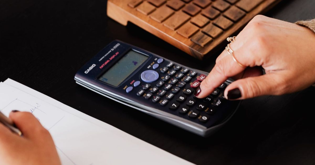 Bookkeeper using a calculator while writing figures on paper
