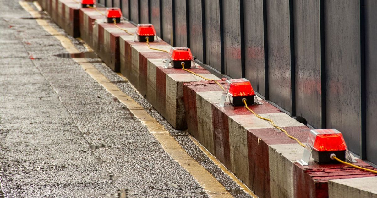 Row of construction barriers with red warning lights along a footpath