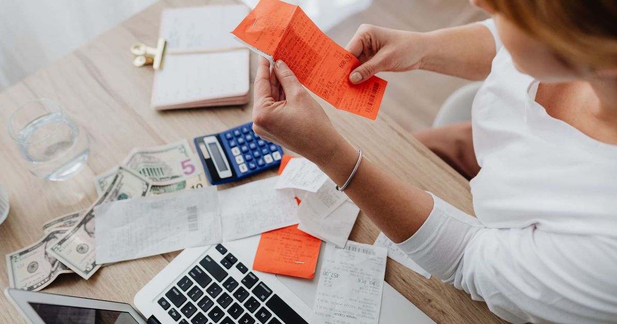 Person sorting receipts at a desk with a calculator and laptop