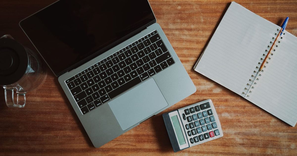Overhead view of a laptop, calculator and notepad on a timber desk